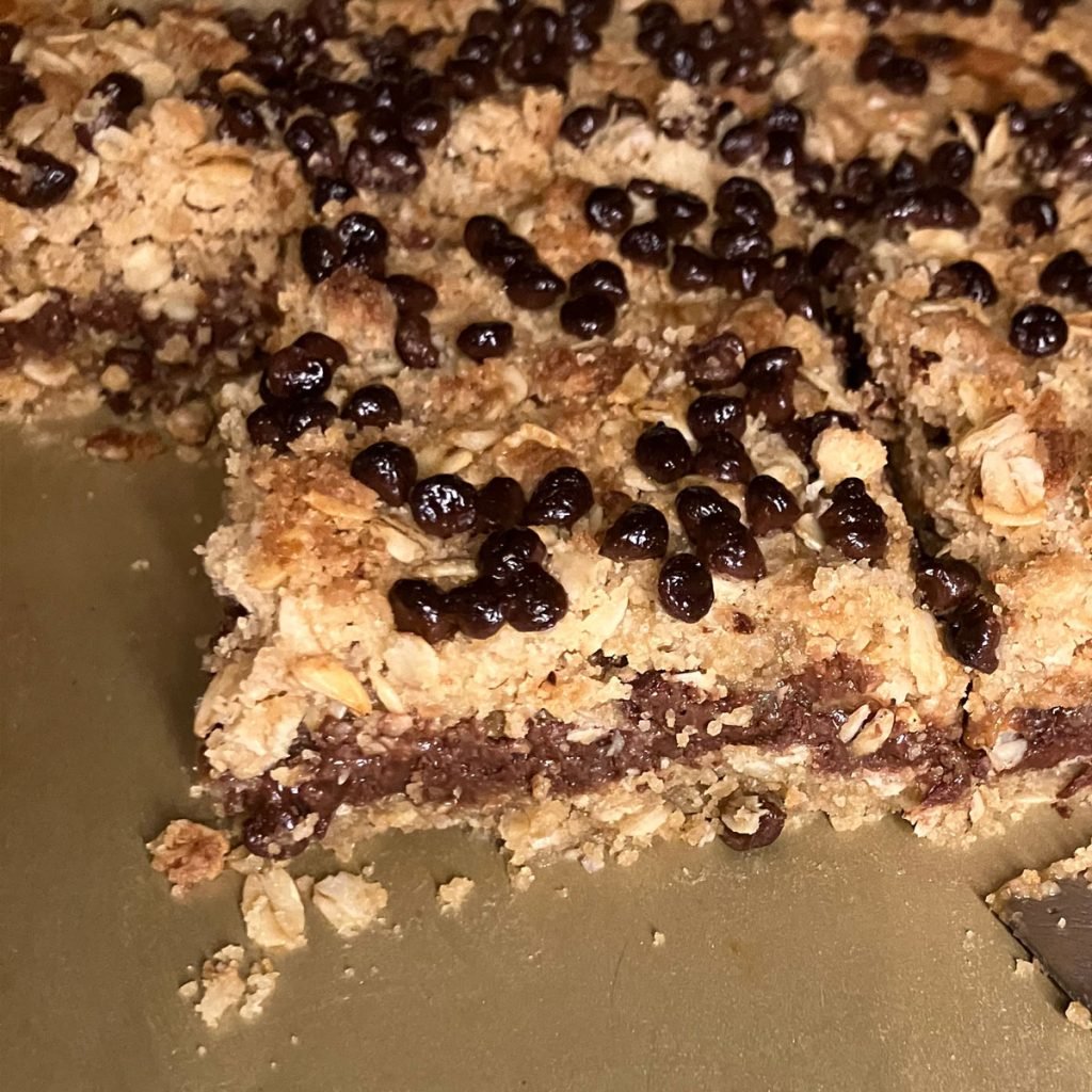 Photo of Caramel, Chocolate Chip, Pecan Bars in a pan. One is being lifted out with a spatula.